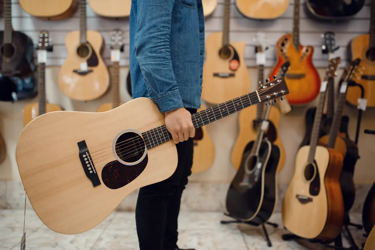 Young man holding acoustic guitar in music store
