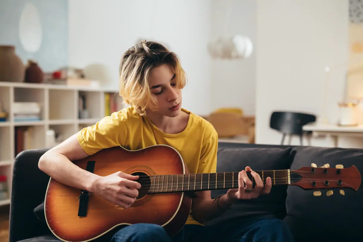 teenager boy learning acoustic guitar at home