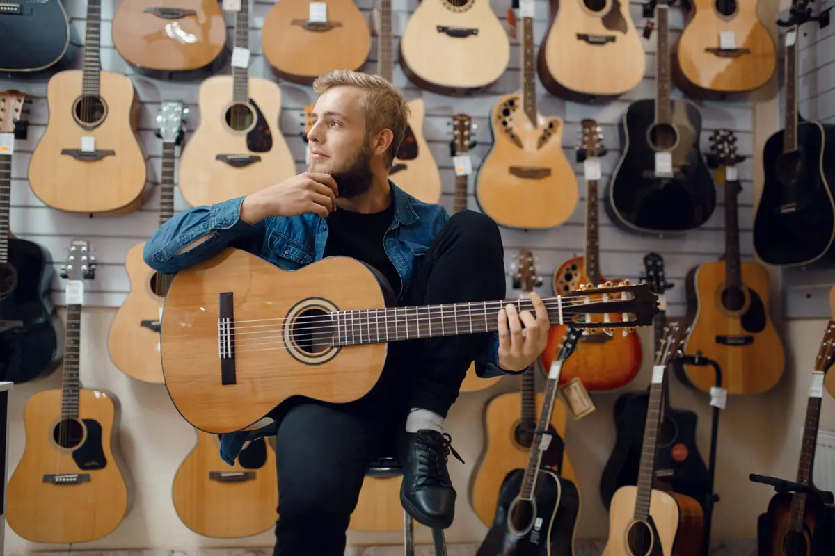 Young man choosing acoustic guitar in music store