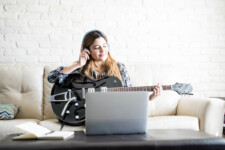 Young woman listening a new tune on headphones while playing a guitar at home