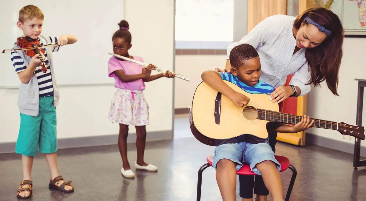 Teacher helping young boy to learn guitar