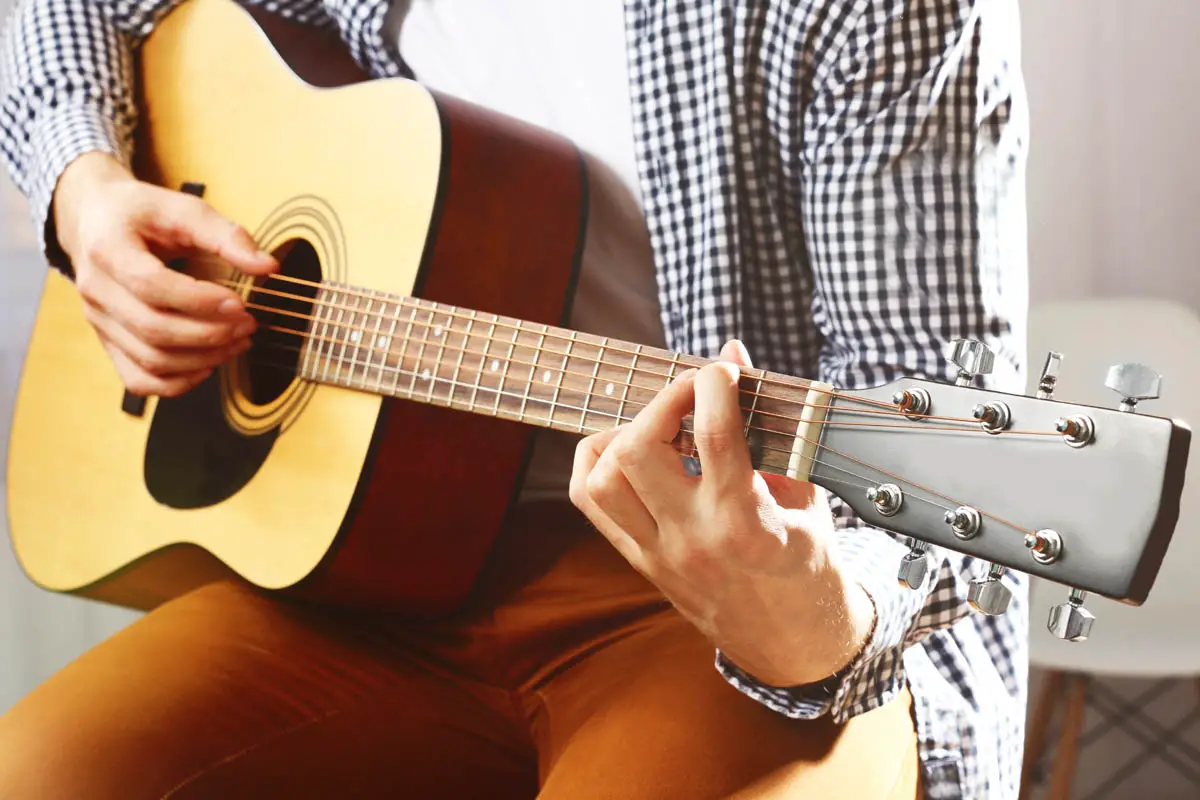 Man with checkered shirt playing acoustic guitar while sitting